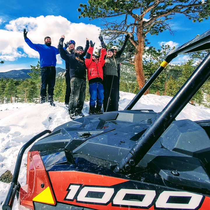 Four people standing in the snow behind a rented SUV.