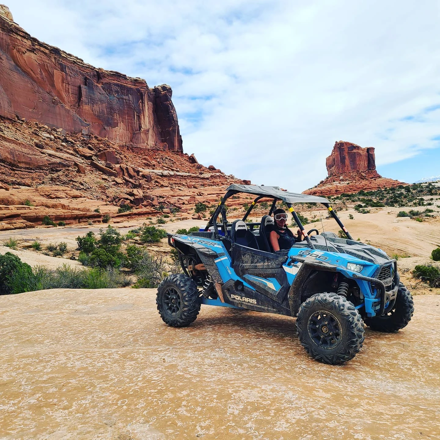 A blue ATV sits on a sand dune as a butte stands in the background